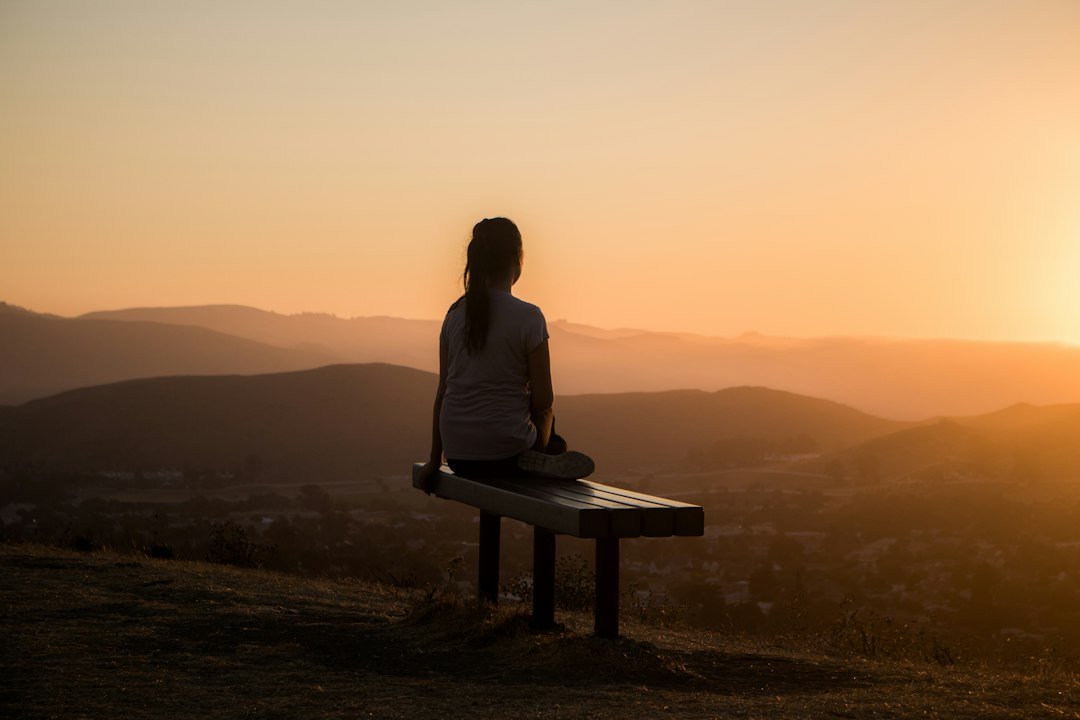 Personne assise en méditation face à un paysage au soleil couchant.